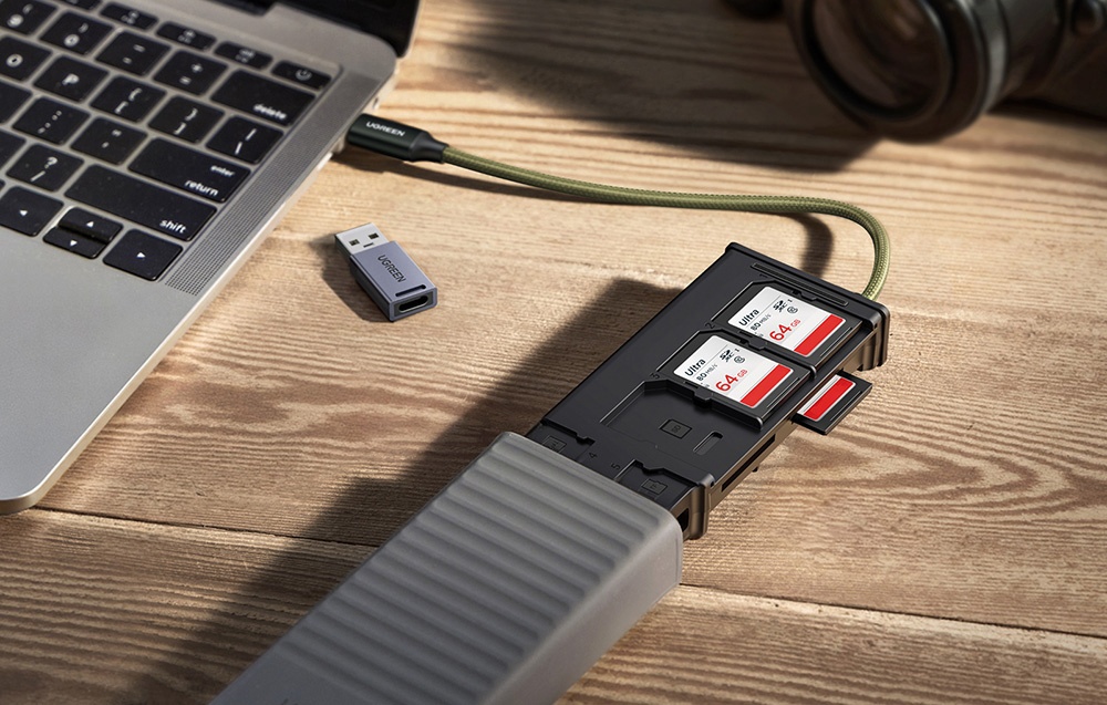 Gros-plan al unui laptop cu un hub USB conectat, în care sunt introduse trei carduri de 64 GB