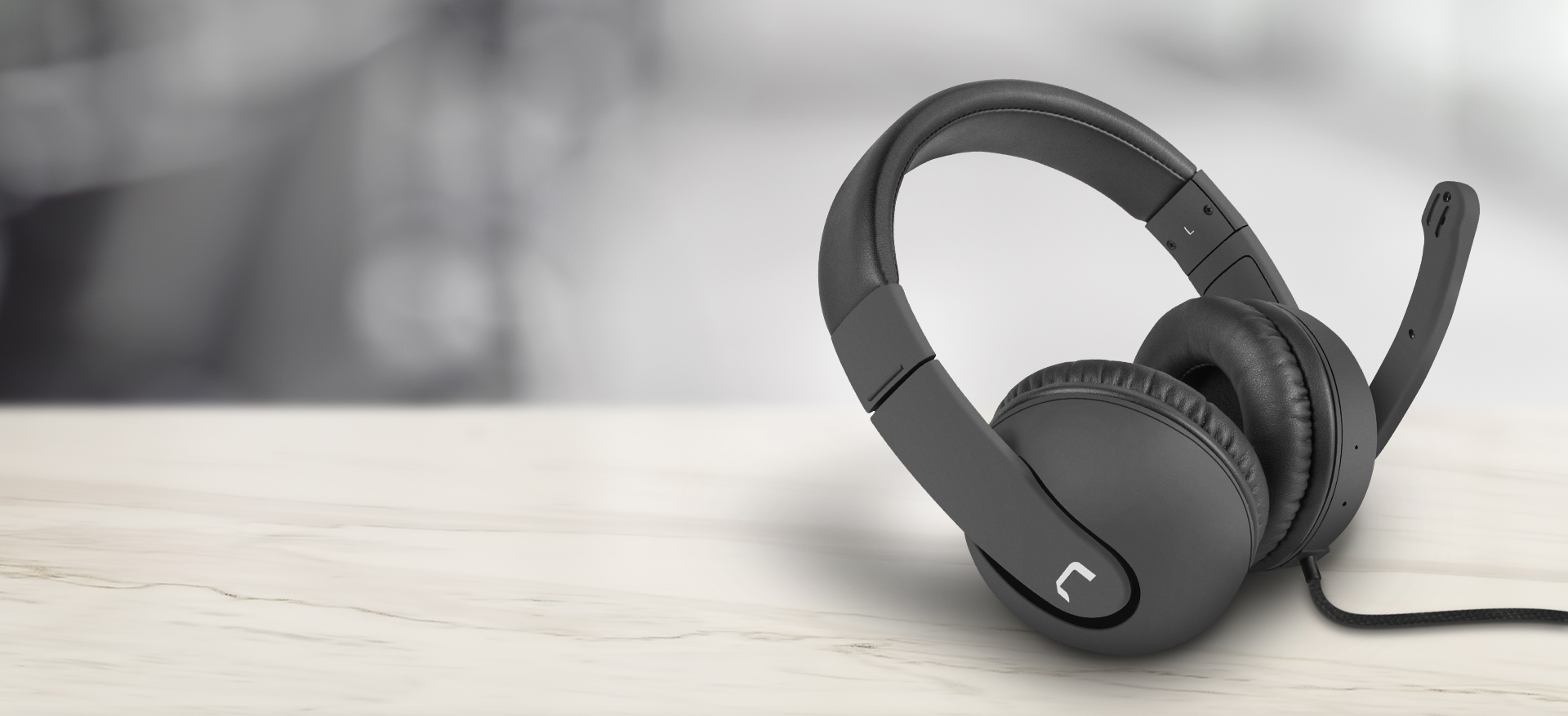 Casti over-ear negre cu microfon, cu design elegant si banda reglabila pentru cap, asezate pe o suprafata din lemn deschis la culoare