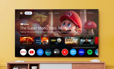 Televizor mare montat pe perete, afisand interfata Google TV, cu filmul The Super Mario Bros. Aplicatii de streaming afisate dedesubt.