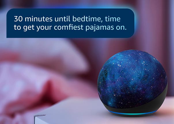Echo Dot Kids 4-inch spherical speaker with galaxy design on bedside table. Text reads: "30 minutes until bedtime, time to get your comfiest pajamas on.